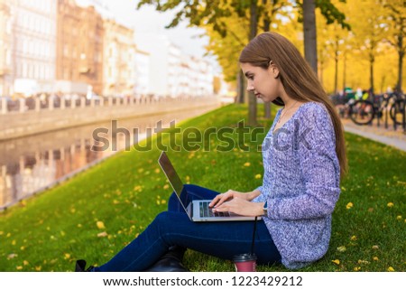 Young caucasian woman smart university student having online learning via portable laptop computer while sitting on a campus during free time in autumn day. Female checking e-mail via netbook device
