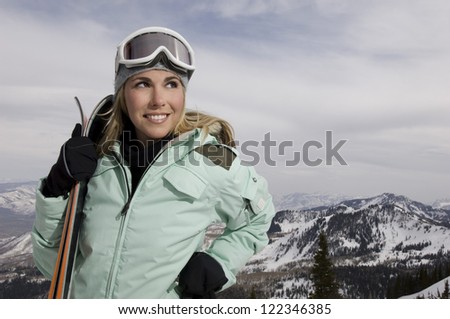 Happy female skier with skis standing at snowy landscape