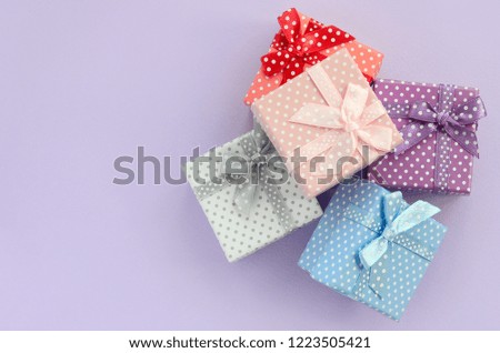 Pile of a small colored gift boxes with ribbons lies on a violet background. Minimalism flat lay top view