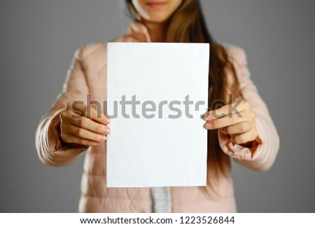 A woman in a warm winter jacket holding a white leaflet. Blank paper. Close up. Isolated background.