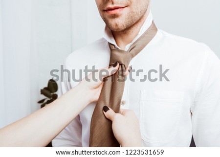 cropped image of woman tying neck tie to boyfriend in white shirt at home