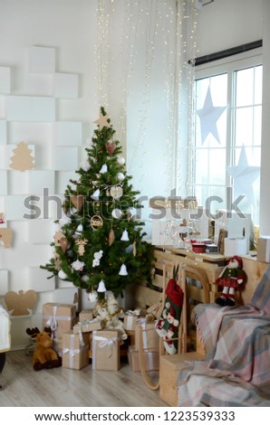Christmas tree in the interior, decorated with toys, under the Christmas tree boxes with gifts, on the walls are white decorative stars.