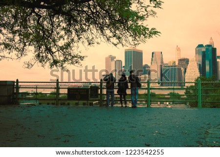 Three people watch Manhattan from Brooklyn. Retro look, green orange tinting.
