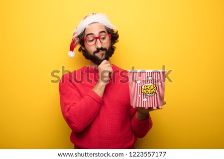 young crazy bearded man wearing santa claus hat, red sweater and glasses expressing a concept against yellow background
