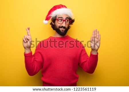 young crazy bearded man wearing santa claus hat, red sweater and glasses expressing a concept against yellow background
