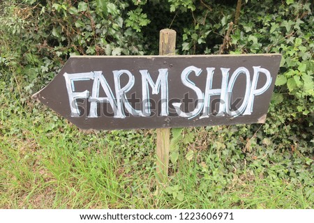 farm shop directional arrow wood posted sign besides green hedges and grass.