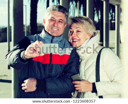 Positive mature couple doing selfie with each other walking on sunny day
