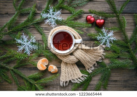 Beautiful cozy Christmas picture with a mug of hot tea in a scarf with fir branches, hearts, snowflakes, tangerine on a wooden background