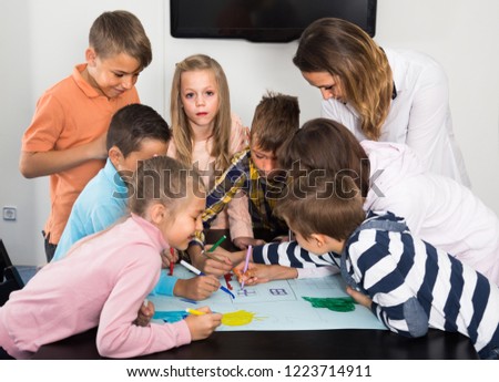 Professor and elementary age children drawing together one picture in school