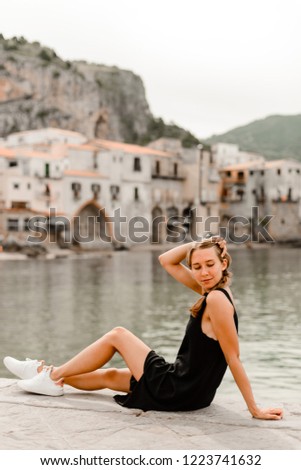 Blonde Girl model posing in black dress in front of italian old city and sea with many colored houses
