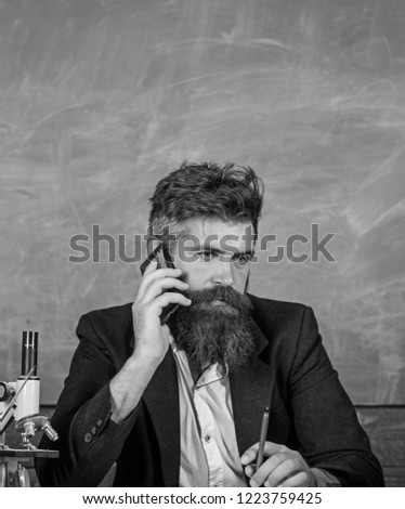 Keep in touch. School teacher call mobile phone while sit classroom chalkboard background. Pedagogue keep in touch with colleagues. Teacher bearded man talk mobile phone. Call colleague ask advice.