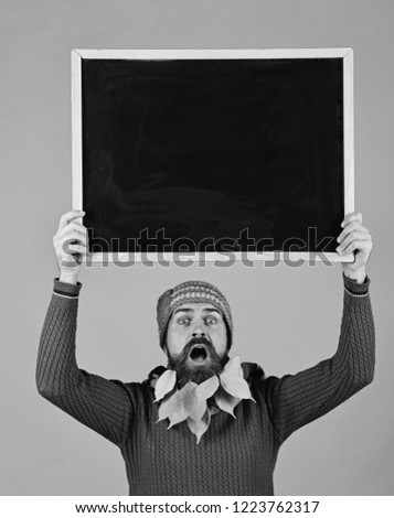 Brutal caucasian or serious hipster with leaves in beard and moustache holding blank blackboard on green background. Bearded man with long beard