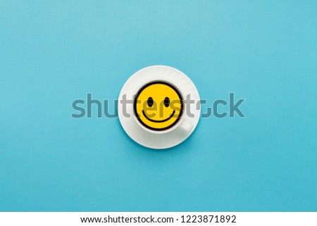 White cup on a saucer, black coffee, blue background. Badge Yellow face with a smile. Flat lay, top view
