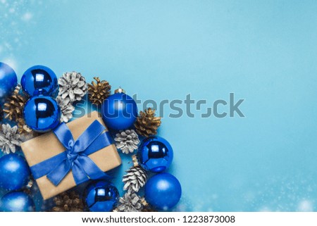 Gift box with blue ribbon, Christmas-tree decorations, balls and white and gold pine cones on a blue background. Concept of Merry Christmas and Happy New Year. Minimalism. Flat lay, top view
