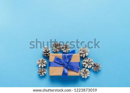 Gift box with blue ribbon and pine cones on a blue background. Minimalism. Flat lay, top view