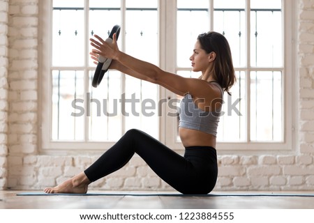 Sporty woman doing pilates toning exercise for arms and shoulders with ring, fitness with pilates magic circle in hands, working out wearing sportswear, indoor full length, white yoga studio or gym Royalty-Free Stock Photo #1223884555