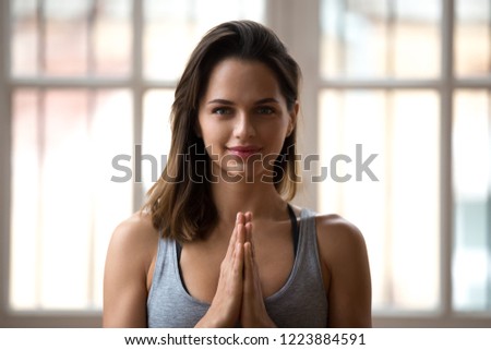 Head shot portrait of beautiful smiling sporty woman doing namaste, yoga, pilates or fitness instructor, attractive female coach wearing sportswear, grey top, looking at camera. Well-being concept