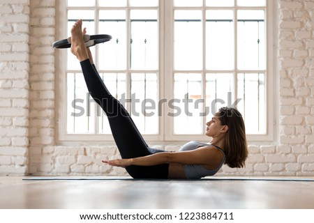 Young sporty attractive woman doing toning pilates the hundred exercise for abs with fitness circle, crunches for abdominal strength using pilates magic circle, practicing at yoga studio or at home Royalty-Free Stock Photo #1223884711