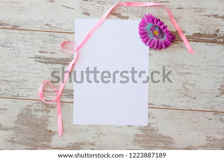 Flat lay with white sheet and pink gerbera and pink satin ribbon on wooden background top view toned picture