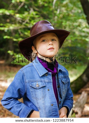 Caucasian schoolgirl in cowboy hat walking in the forest, sunny