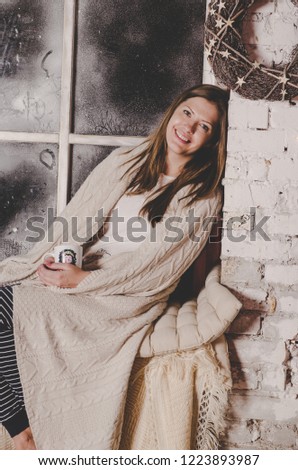 Beautiful young woman sitting near Christmas decorated window with cozy blanket 