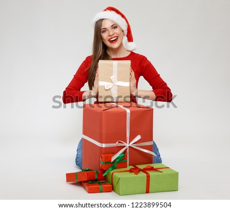 Portrait of woman wearing christmas santa hat sitting on floor with pile of gift boxes.