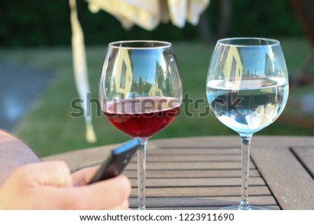Man using smartphone. Half full red wine glass. Half full water glass. Drinking choice concept with man.  Garden