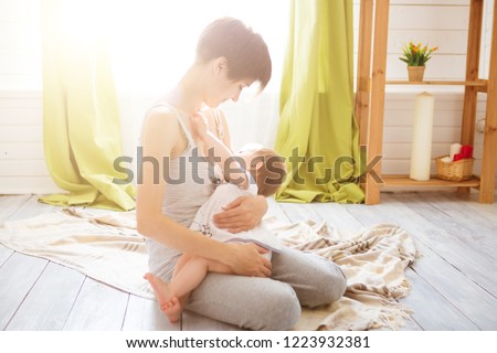 Young caucasian mom with infante in interior location. Mom nursing baby in a white bedroom. Nursery interior. Family at home.