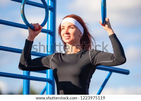 Sport Ideas. Concentrated Caucasian Sportswoman in Summer Black Outfit Having Exercises on the Rings Outdoors. Horizontal  Image Orientation