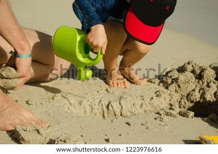 A small child in a cap pours water from the watering can of sand on the beach
