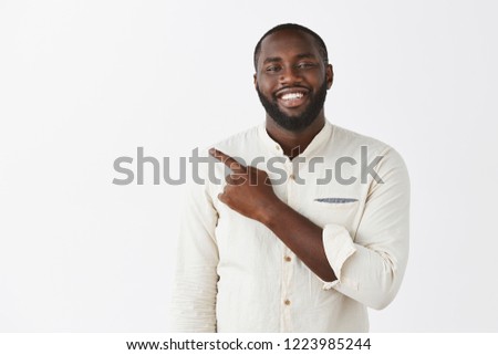 Proud and satisfied handsome African-american businessman pointing left as showing chart being delighted and happy present project of team smiling broadly at camera as posing over gray background