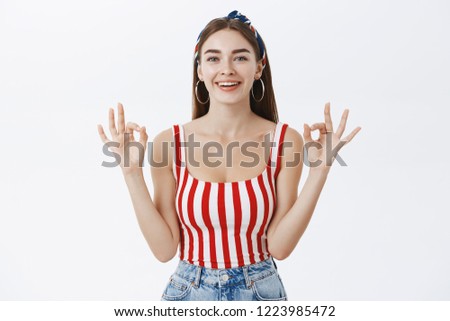 Everything fine, rely on me. Confident attractive young woman in striped top and headband showing okay gesture with both hands and smiling, giving approval or telling has everything under control