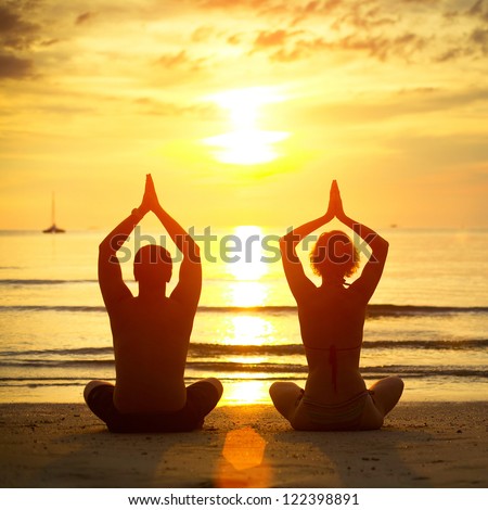 Young couple practicing yoga on the beach at sunset