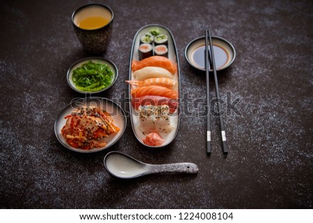 Asian food assortment. Various sushi rolls placed on ceramic plates. Kimchi and goma wakame salads. Soy souce and chopsticks on sides. Grungy dark background with copy space.
