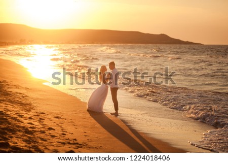 happy beautiful young couple in wedding dress and suit by the sea at sunset, waves
