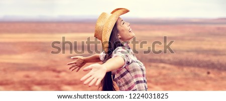 Cowgirl american woman happy with open arms in freedom wearing cowboy hat enjoying outback background panorama banner. Beautiful smiling multiracial Caucasian Asian young woman, Arizona Utah, USA.