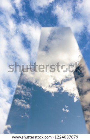 Vertical abstract view of the blue cloudy sky reflected on triangular towers of mirrors. Reflective geometric shapes angled up towards the sky. Its surface mirrors the ever-changing environment
