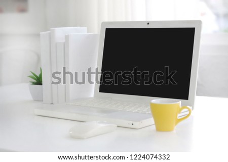 Coffee mug and laptop with blank screen. White table