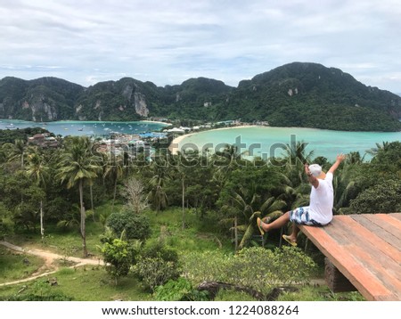 Young tourist sitting and rises hand enjoying amazing view on the top mountains at Phi Phi Island View Point,Thailand. holiday travel vacation adventure concept