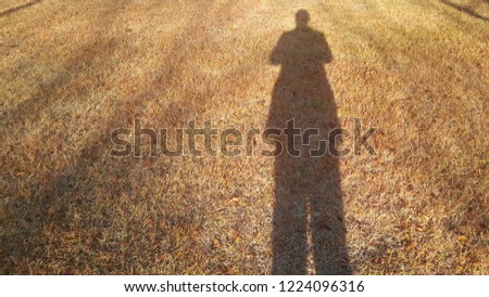 Man's shadow on a brown grass playground with sun light from backside
