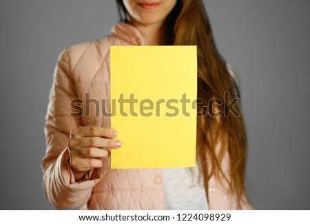 A woman in a warm winter jacket holding a yellow leaflet. Blank paper. Close up. Isolated background.