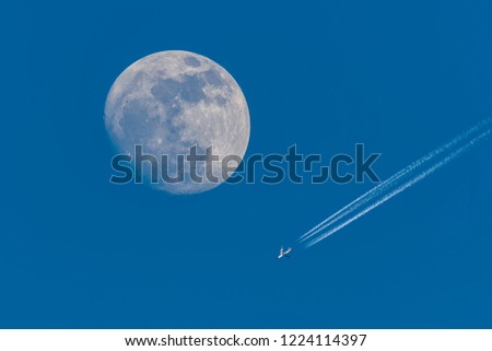Full moon and flying plane with clear blue sky.