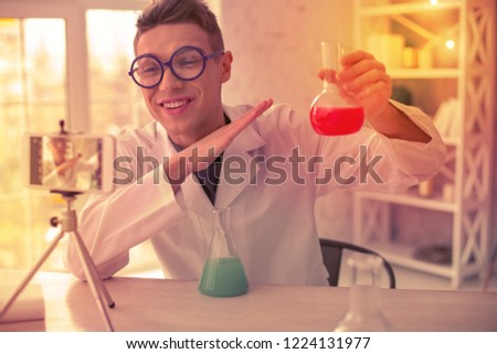Beaming chemist holding. Beaming chemist holding test tube in one hand while recording educational video