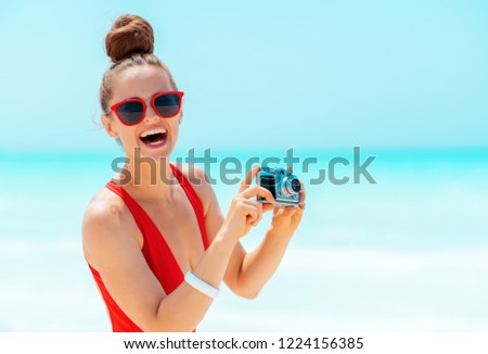 Portrait of smiling modern woman in red swimwear with retro photo camera on the seacoast