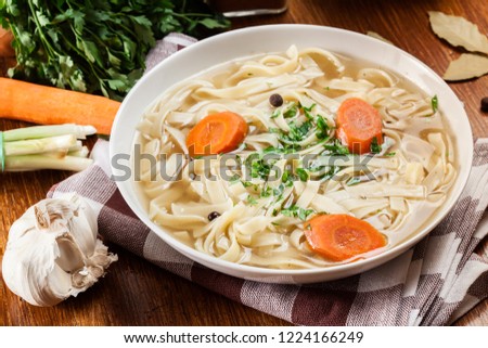 Tasty meat broth with noodles, carror and parsley in a plate
