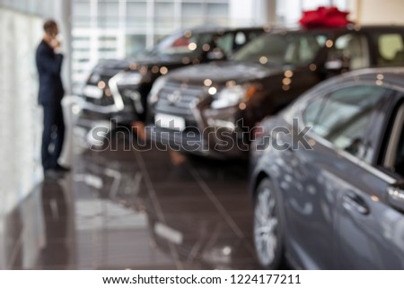 Customer ponders buying a new car. Modern and prestigious vehicles. Themed blur background with bokeh effect.