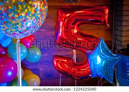 Bright red inflatable balloon next to other balloons with the number five.
