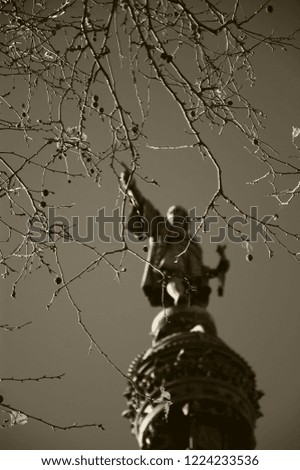 Blurry Columbus Monument at La Rambla, (Barcelona, Catalonia, Spain) seen through bare twigs with last autumn leaves. It was built in honor of Columbus first voyage to the Americas. Sepia photo.