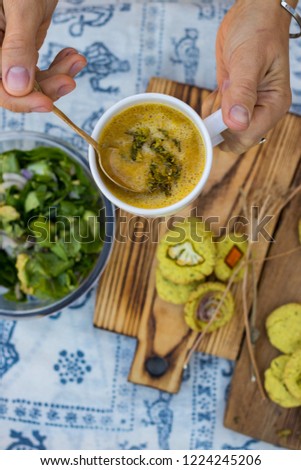 Woman hands holds spoon with hot broth vegetable soup in white cup with herbs, spices and greens. Fresh spinach avocado salad and corn turmeric bread with vegetables. Paleo vegan diet