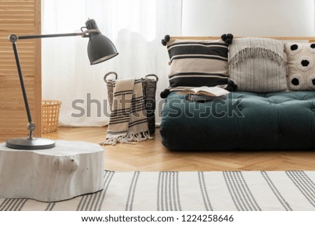 Scandinavian futon with patterned pillows in natural interior with white wall and parquet on the floor, real photo